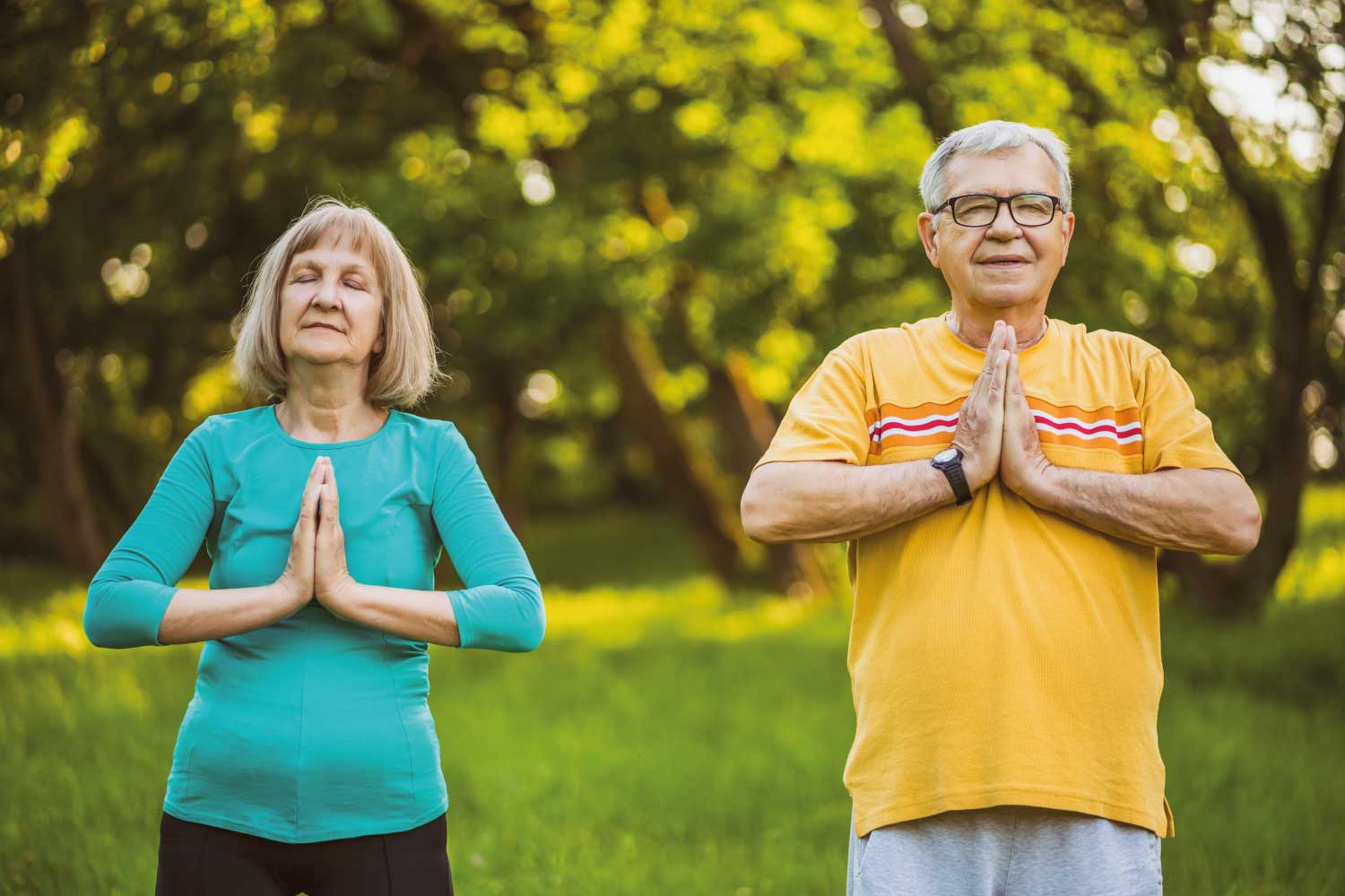 Elderly couple peacefully doing meditation yoga outside in summer.