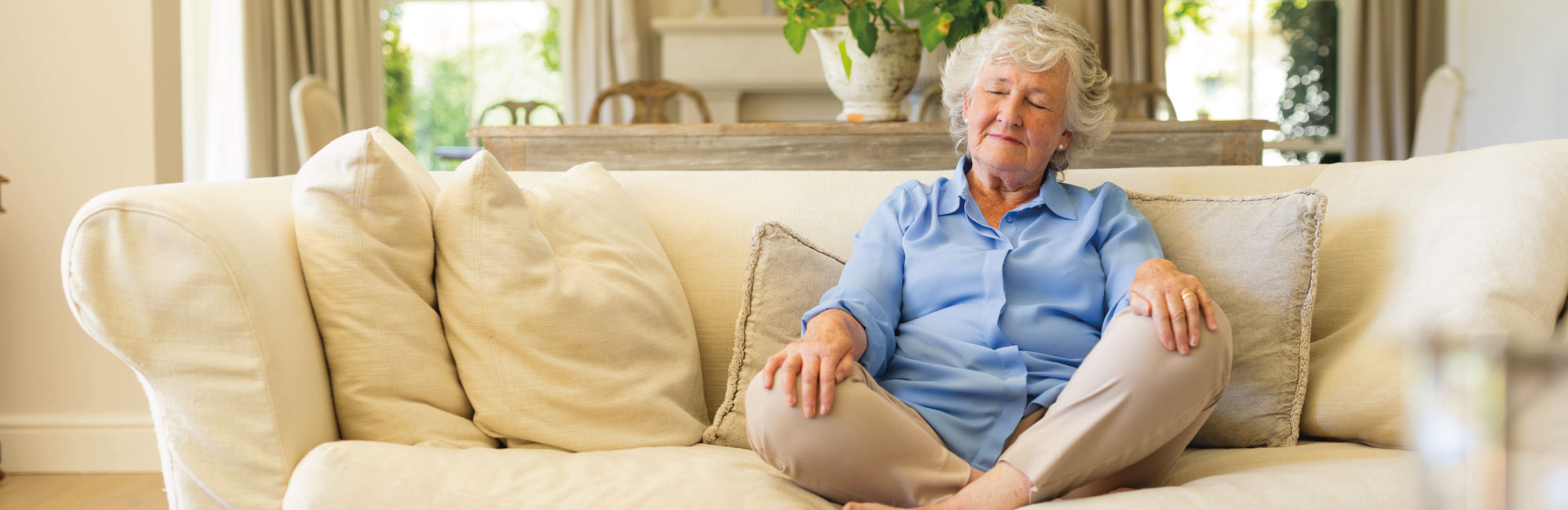 Middle-class elderly woman meditating on her sofa.